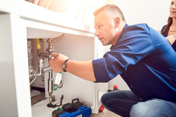 Obraz premium Plumber work with pipes under the sink and show owners where the problem is in the pipe under the sink