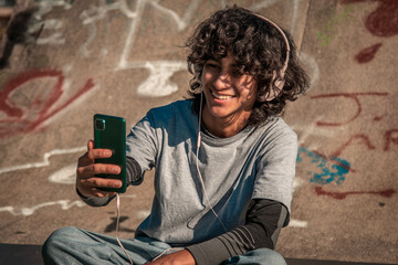 smiling man teenager with headphones and skateboard at skate park