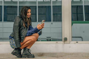 young latin hispanic woman using phone crouching on the street