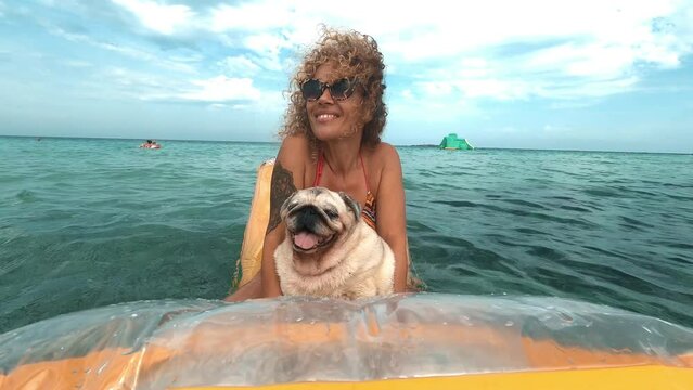 Happy woman have fun on vacation playing and relaxing on a yellow inflatable lilo with her dog pug on it and looking on camera. People and animal lifestyle. Vacation with dog and outdoor leisure