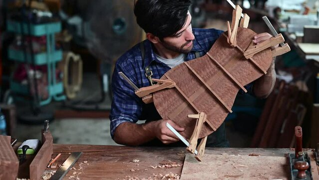 Luthier creating a guitar and using tools in a traditional, clamps on the body of a guitar under construction improving glue adhesion