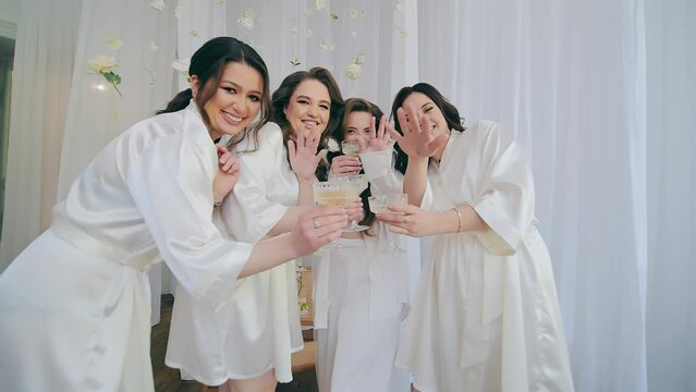 Wedding morning of the bride. The girls pose in front of the camera. They drink wine and wave at the camera