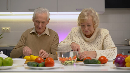 Smiling senior woman and man cutting fresh vegetables in the kitchen, living a healthy lifestyle