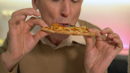 Close-up of a senior man biting a slice of pizza, enjoying Italian cuisine at home