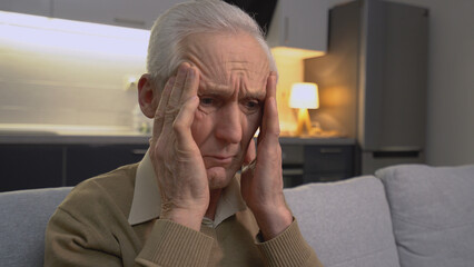 A senior Caucasian man feeling a headache and massaging his temples, elderly health care