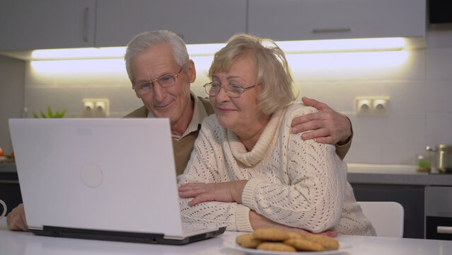 Smiling grandparents talking to their grandchildren using an app on a laptop for a video call
