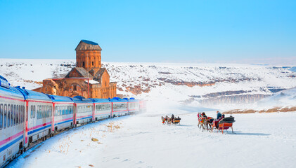 Red diesel train (East express) in motion at the snow covered railway - Horses pulling sleigh in...