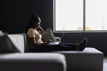 Woman sitting on living room couch working remotely from home using laptop