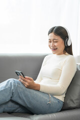 Asian woman with braces sits online shopping on sofa with laptop. mobile phone and credit card in hand