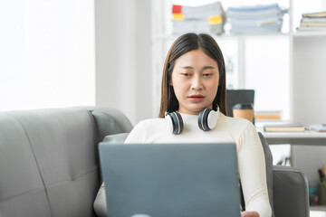 Asian woman with braces sits online shopping on sofa with laptop. mobile phone and credit card in hand