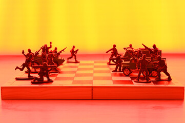 Concept of military aggression on the chessboard. Toy soldiers and military vehicles are fighting against each other. Red glow.