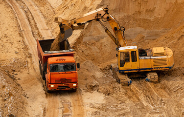 excavator extracts and loads sand into large truck in sand quarry