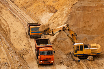 excavator extracts and loads sand into large truck in sand quarry