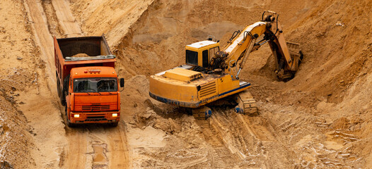 excavator extracts and loads sand into large truck in sand quarry