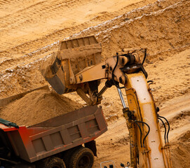 excavator extracts and loads sand into large truck in sand quarry
