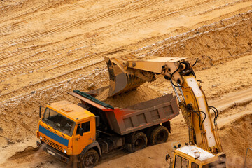 excavator extracts and loads sand into large truck in sand quarry