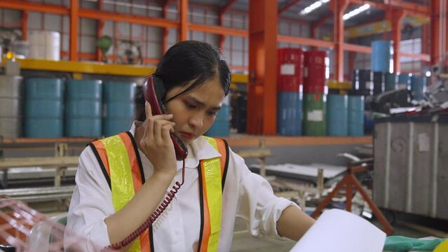 Asian Woman working in an industrial, Female industrial worker, Taking phone call and referencing document to provide necessary information.