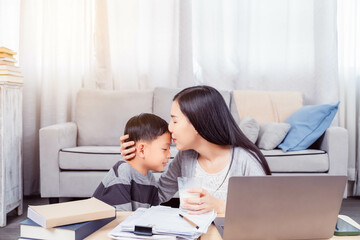 Asian little boy or son give glass of milk to his mom for her healthy at home after work Asian Mother kiss son for thank you during Single Mom work from home by using laptop computer at living room