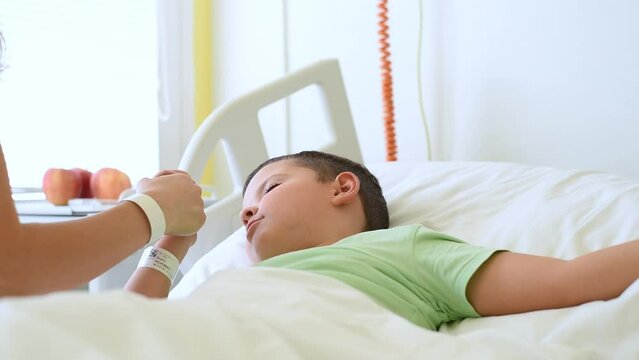 A caring young mother kisses her little son as he lies in a hospital bed.