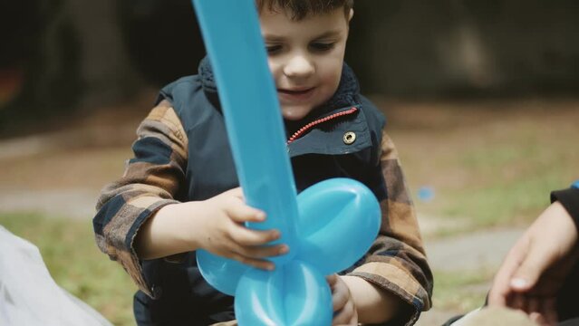 portrait of a little cute boy. outdoor kid's party. a boy plays with inflatable in the form of a sword balloon. in the park, warm summer day
