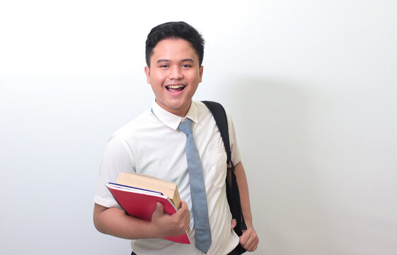 Indonesian Senior High School Student Wearing White Shirt Uniform With Gray Tie Holding Some Books, Smiling And Looking At Camera. Isolated Image On White Background