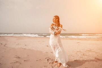 woman sea white dress. Model in boho style in a white long dress and silver jewelry on the beach. Her hair is braided, and there are many bracelets on her arms.