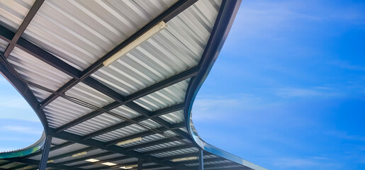 Modern corrugated metal curve roof of covered walkway with black steel roof beam structure against blue sky background, view from below and panoramic view