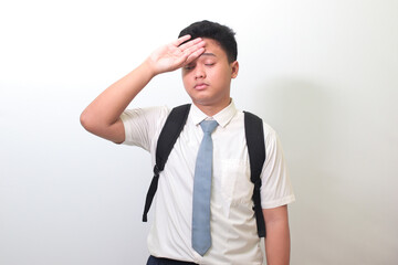 Indonesian senior high school student wearing white shirt uniform with gray tie suffering headache and holding hands on forehead. Isolated image on white background