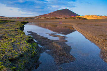 Fototapeta na wymiar Tranquil Dawn: El Médano's Golden Hour with Waves, Rocks, and Sand