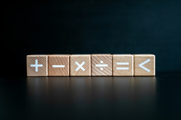 Wooden block written "+, -, x, ÷, =, less than" with a black background.