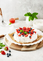 Delicious homemade Pavlova cake with fresh strawberries, blueberries, raspberries, whipped cream and strawberry sauce. Sweet food concept. Copy space.