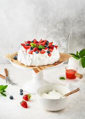 Homemade Anna Pavlova cake with fresh strawberries, blueberries, raspberries, vanilla cream and strawberry sauce. Summer meringue dessert recipe, menu. 
