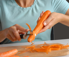 Young woman peeling fresh carrots on kitchen cooking table.