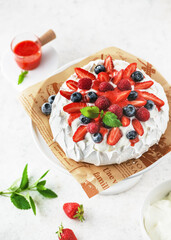 Top view of homemade delicious meringue cake Pavlova with whipped cream, fresh strawberries, blueberries, raspberries and strawberry sauce.  Sweet food concept. 
