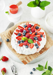 Traditional Pavlova cake with fresh strawberries, blueberries, raspberries, whipped cream and strawberry sauce. Homemade sweet food concept. View from above.