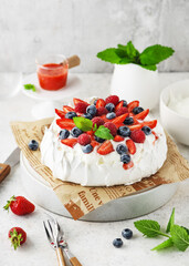 Homemade sweet and creamy Pavlova cake with fresh berries, vanilla cream and strawberry sauce. Summer meringue dessert recipe, menu. Copy space.