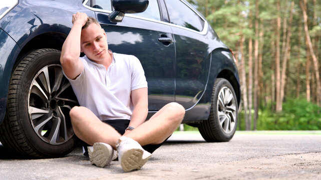 Young sad upset frustrated man driver sitting near his broken car