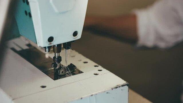 Tailor repairing white fabric in workshop, dressmaker preparing thread and needle of sewing machine before creating seam on textile, work in atelier and seamstress business