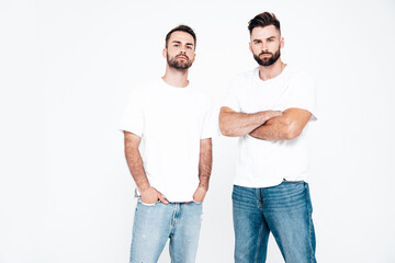 Portrait of two handsome confident stylish hipster lambersexual models. Sexy men dressed in white T-shirt and blue jeans. Fashion male isolated on white background in studio