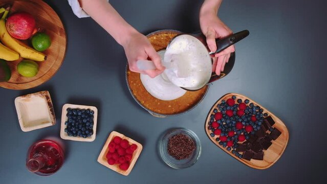 Woman pouring liquid yogurt cream on cake. Top view of kitchen table. Cooking in the kitchen.