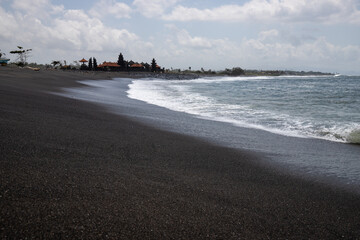 Black sand beach in Bali, natural with temples, boats (jukung) and waves at sunrise. Tropical...
