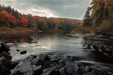 Raquette River in Long Lake, NY, Adirondacks, surrounded by vivid fall foliage on an overcast afternoon