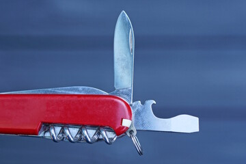 one red folding knife with an open gray blade and a bottle opener on a black background - obrazy, fototapety, plakaty