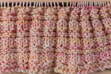hand knitting with a lovely apricot peach wool with texture on plain background with knitting needles 
