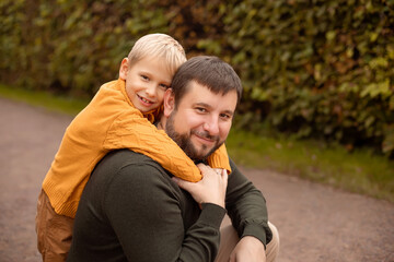 Portrait of dad and son. Son hugs dad tightly, walks in autumn park.