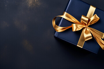 Gift box with golden bow on dark background. Top view with copy space