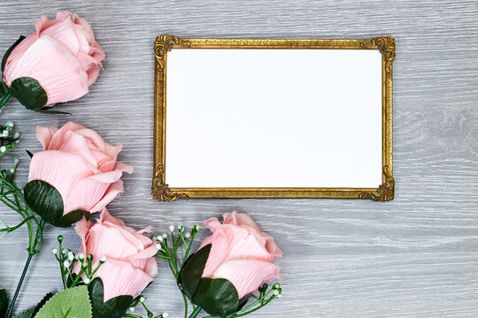 golden picture or photo frame mockup with pink roses flowers on gray wood table