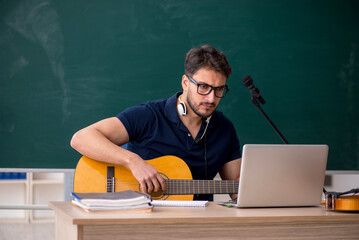 Young male music teacher sitting in the classroom