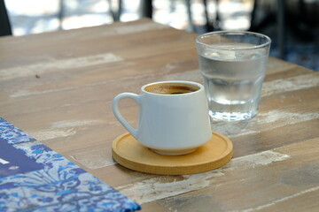 A cup of Turkish coffee, a glass of water and a book on wooden table
