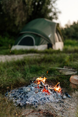 Tent and burning fire among green grass and trees on a summer sunny day. Camping.
